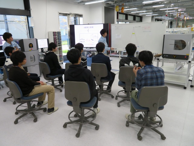 座っている参加者の前でプロジェクタやホワイトボードを使って社員が説明している写真です。