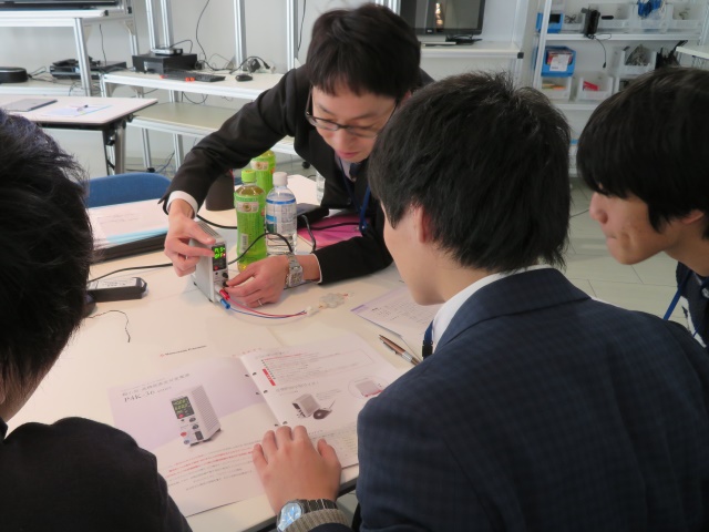 社員１人と参加者３人が座って、製品カタログと見比べながら社員が弊社の直流電源装置を見せて操作説明をしている写真です。